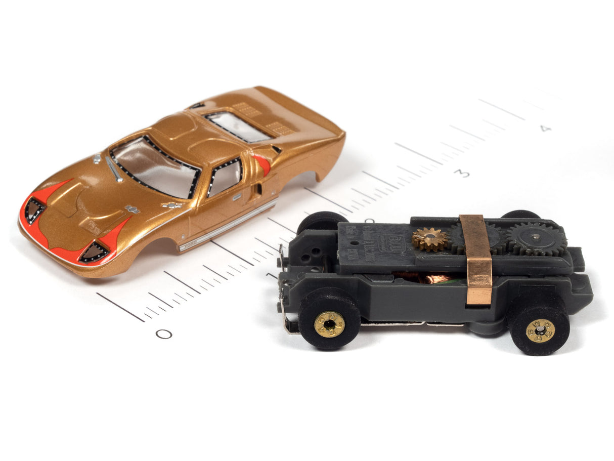 Two slot cars, a gold sports car and a black, boxy vehicle, on a ruler for Auto World SC379
