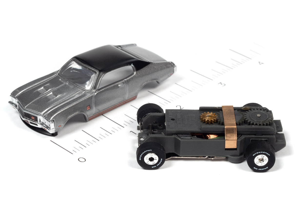 Two slot cars on a ruler: a gray sedan and a black, mechanical vehicle for Auto World SC379