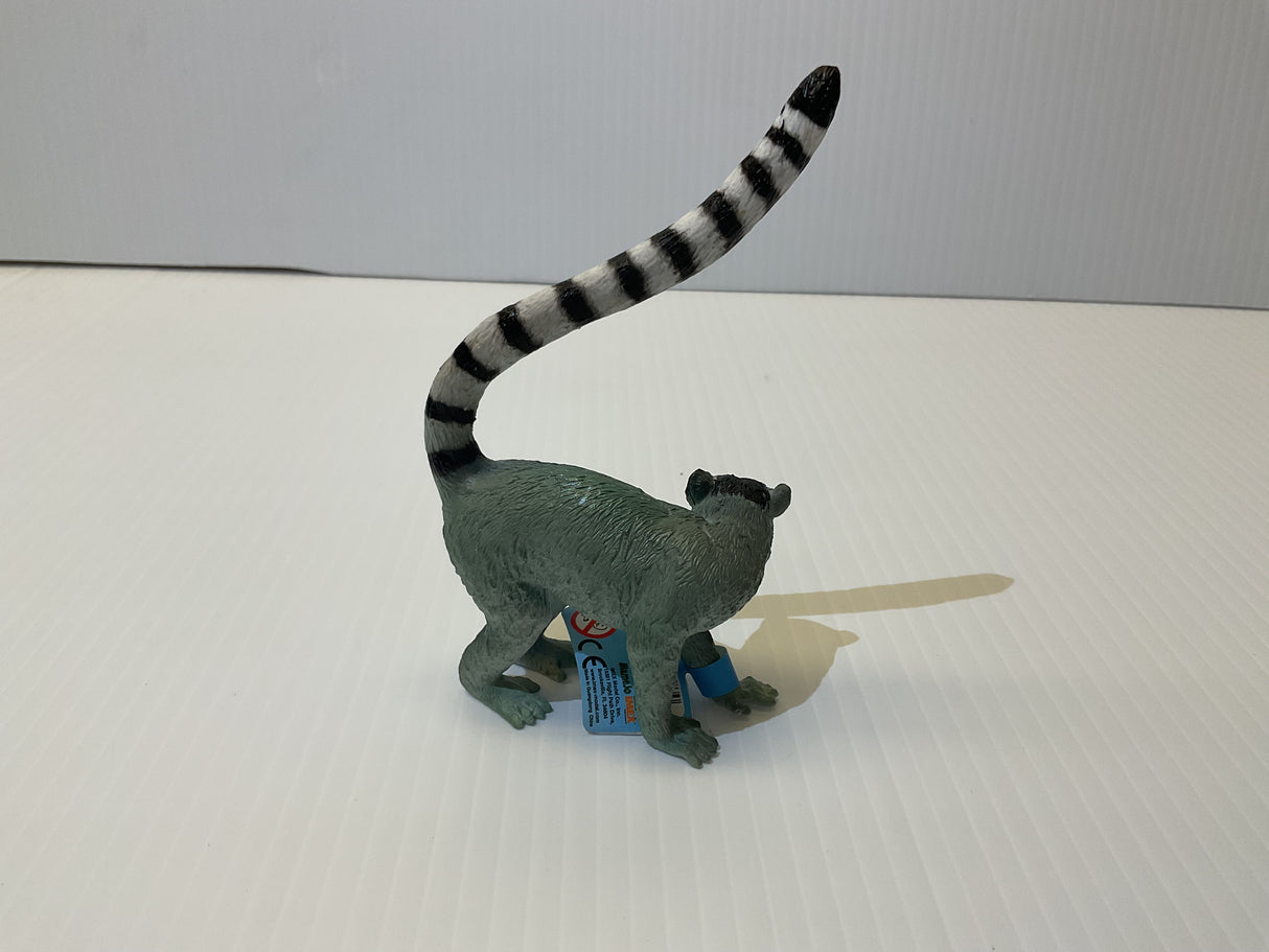 Grey lemur toy with long, striped tail standing on a white surface for Mamejo MAJ55028, rear view