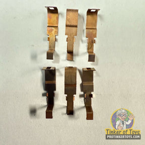 Six metal shoe-shaped pieces, likely for a toy, laid out on a white surface for Tyco 6692