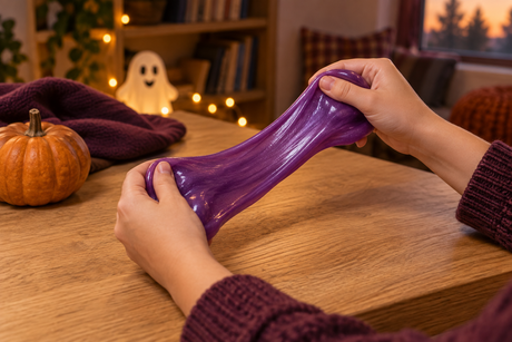 Hands stretching purple putty at a cozy autumn craft table with a pumpkin and friendly ghost decoration