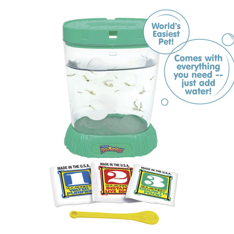 A teal aquarium is filled with water and Sea-Monkeys. Laying in front, there are three packets, numbered 1, 2, and 3 from