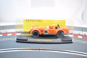 Orange slot car of an AC Cobra race car on a display base for ReproTec RT/1963