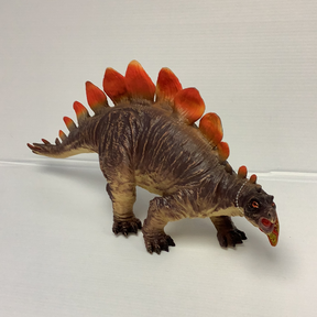 Stegosaurus toy dinosaur with red plates, standing on a white surface for IMEX Model Company IMX49403